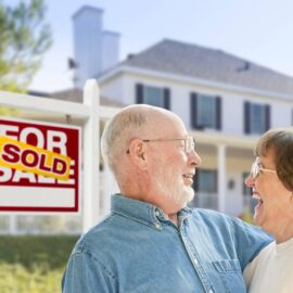 Happy couple standing in front of House Sold sign.